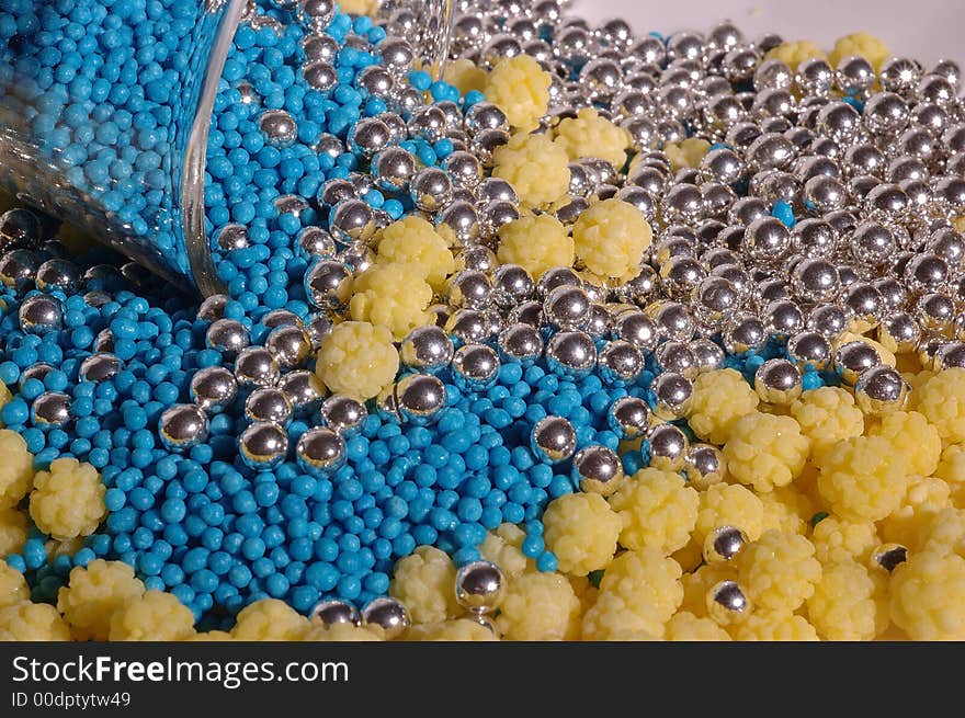 Small blue candies in a small glass on a saucer with yellow and silver candies