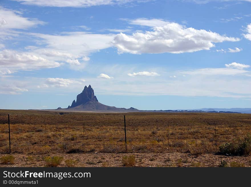 Shiprock monument from far away in New Mexico on a clear day with blue cloudy skies and other rocks in the background. Shiprock monument from far away in New Mexico on a clear day with blue cloudy skies and other rocks in the background