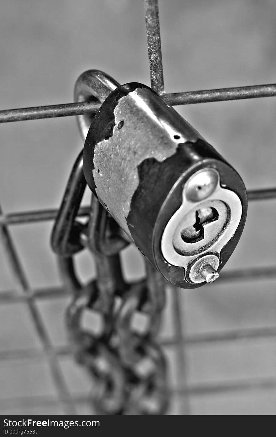 A black and white close up of a metal lock and chain on a fence. A black and white close up of a metal lock and chain on a fence