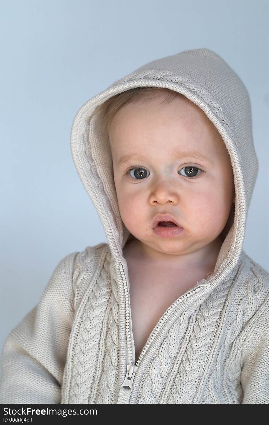 Image of cute baby wearing a hooded sweater, sitting in front of a white background. Image of cute baby wearing a hooded sweater, sitting in front of a white background