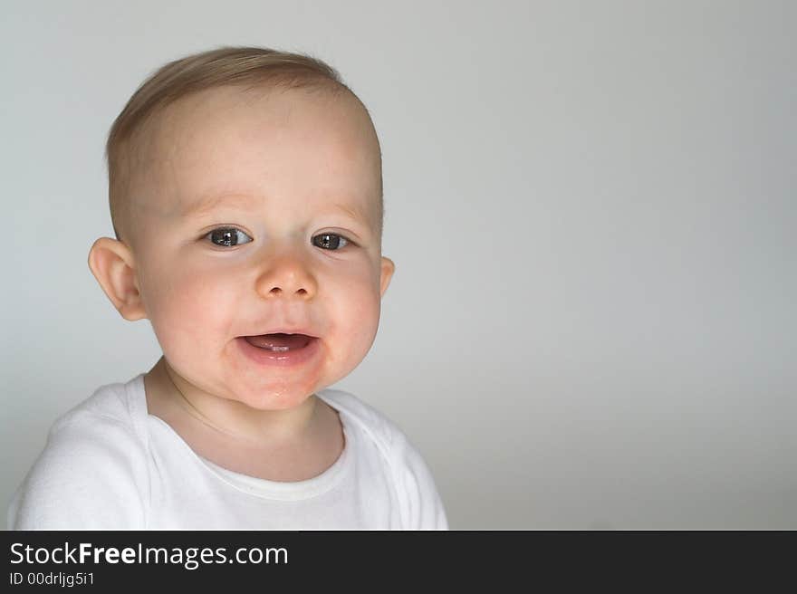 Image of a happy, smiling beautiful baby wearing a white shirt, sitting in front of a white background. Image of a happy, smiling beautiful baby wearing a white shirt, sitting in front of a white background