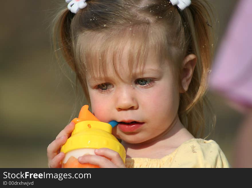 This is a close up of my two year old daughter getting something to drink after she has been playing in the sand. You can see the sand in her hair, and on her face. This is a close up of my two year old daughter getting something to drink after she has been playing in the sand. You can see the sand in her hair, and on her face.