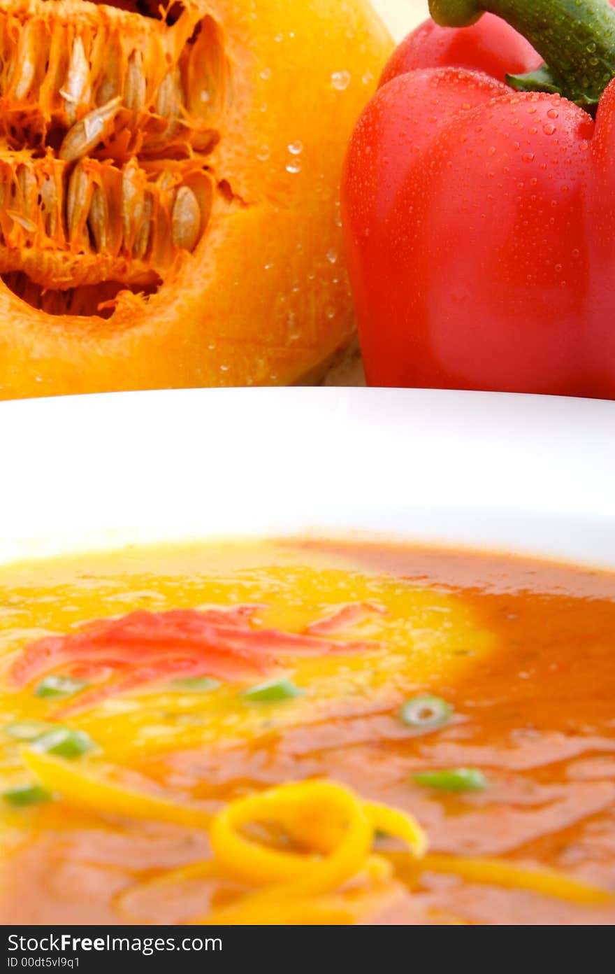 Squash soup and Red Pepper soup in a bowl spiraled together to form a yin yang with fresh vegetables in background.