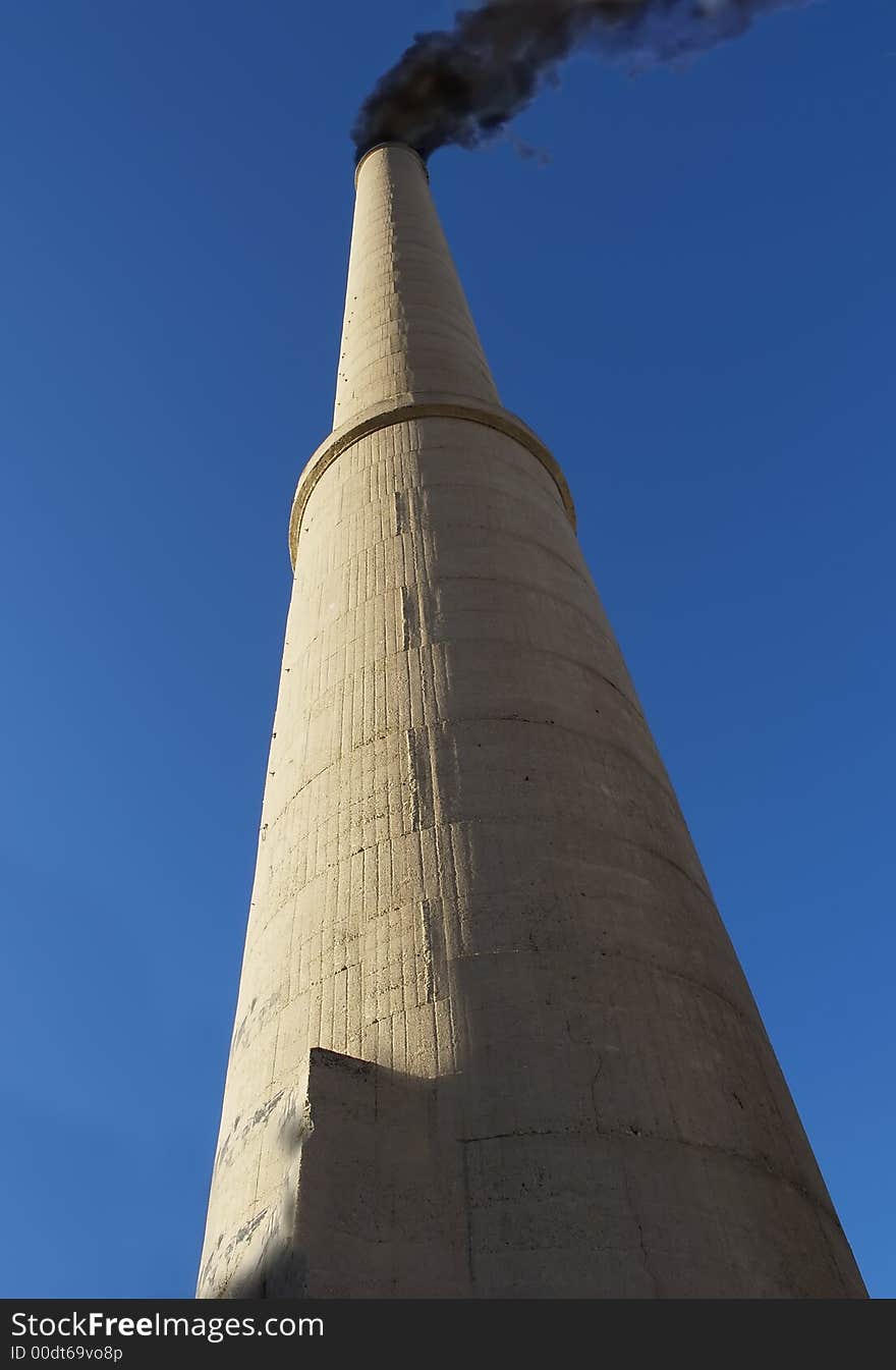 Tall concrete smoke stack and black smoke