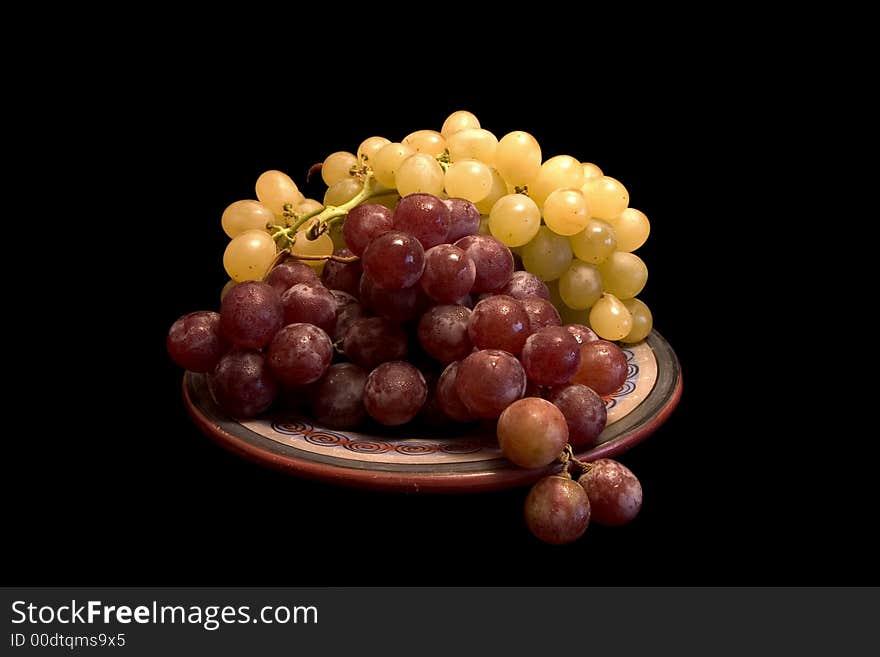 White and black grapes on a plate, isolated on black