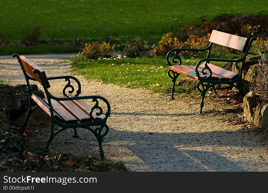 Two facing empty benches in a park at about sunset time. Two facing empty benches in a park at about sunset time.