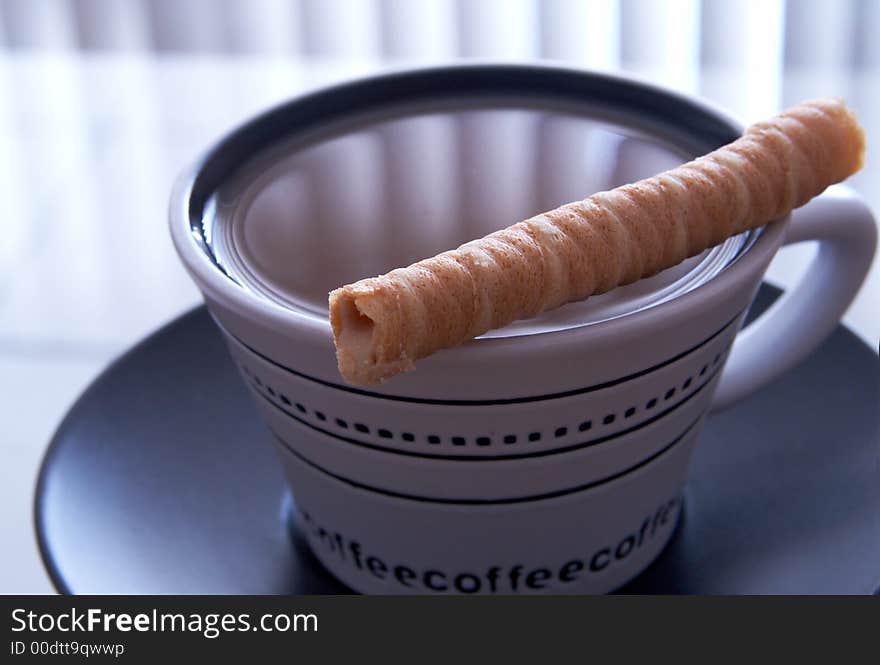 A white cup of coffee on black saucer. A baked swirl is lying on top of the cup. A white cup of coffee on black saucer. A baked swirl is lying on top of the cup.