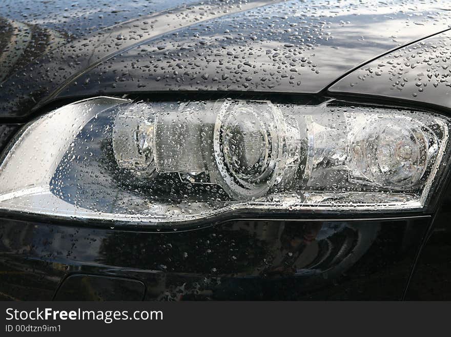 Head lights of a sport black car with drops of rain