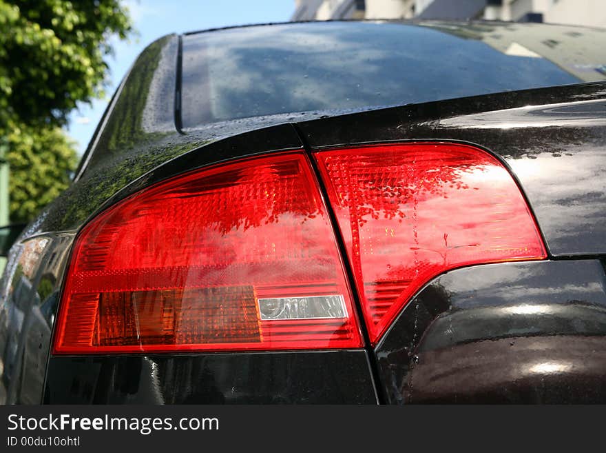 Back lights of a sport black car in blue sky. Back lights of a sport black car in blue sky