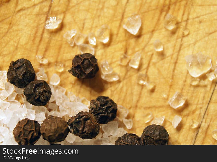 Macro shot of seasalt and whole peppercorns on a wooden chopping board. Macro shot of seasalt and whole peppercorns on a wooden chopping board