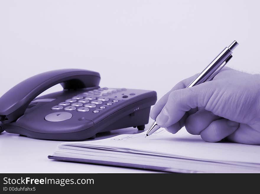 Man holding pen and writing in weekly planner, phone on the background. Man holding pen and writing in weekly planner, phone on the background