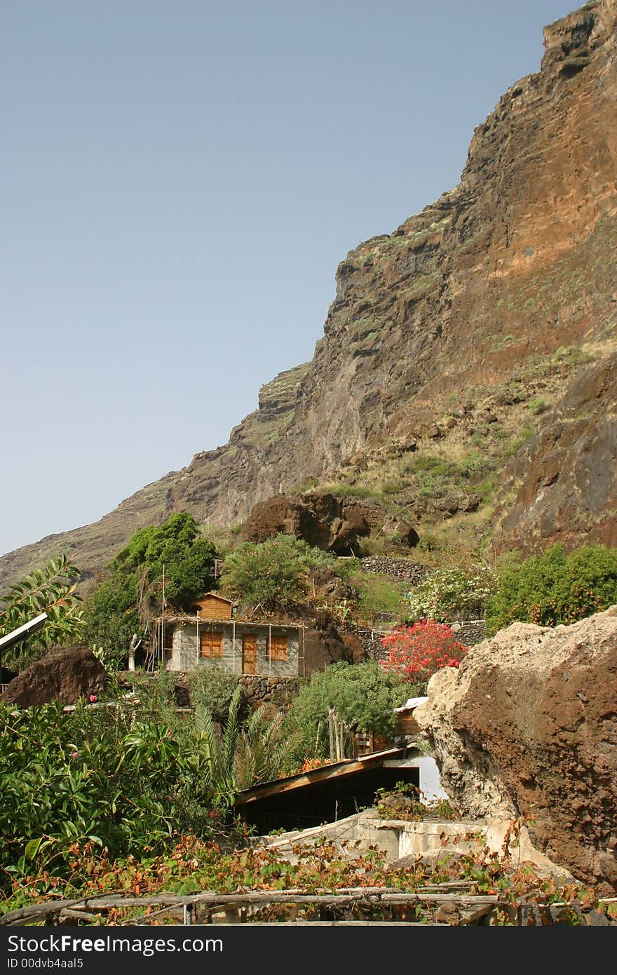 Little house with tropical plants at the bottom of a steep mountain. Little house with tropical plants at the bottom of a steep mountain