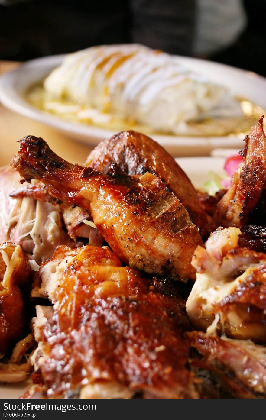 Grilled Chicken lie on a plate in the foreground with a tasty burrito covered in sour cream lies in the background blurred. Grilled Chicken lie on a plate in the foreground with a tasty burrito covered in sour cream lies in the background blurred