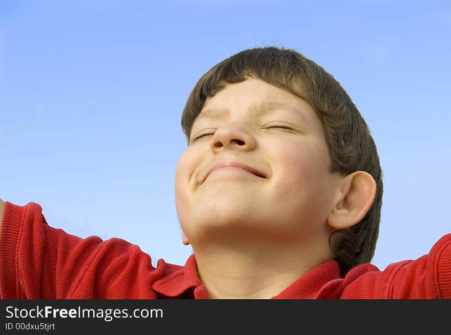 A close-up of a smiling boy tilting his head back against a blue sky and closing his eyes in pleasure. A close-up of a smiling boy tilting his head back against a blue sky and closing his eyes in pleasure.