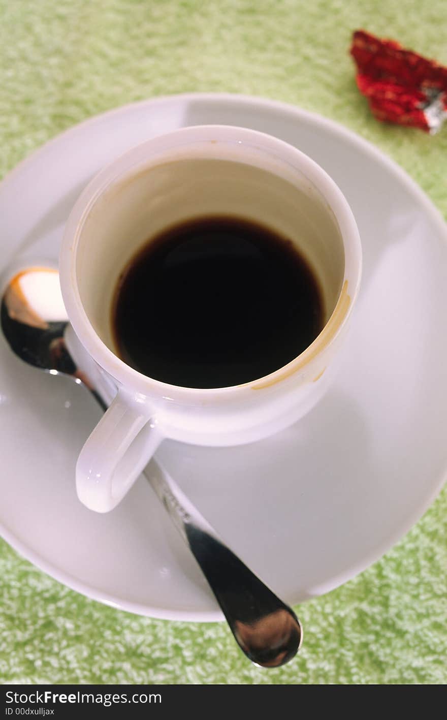 Small cup of coffee with  spoon in  plate and  red wrapper on  green cloth. Small cup of coffee with  spoon in  plate and  red wrapper on  green cloth