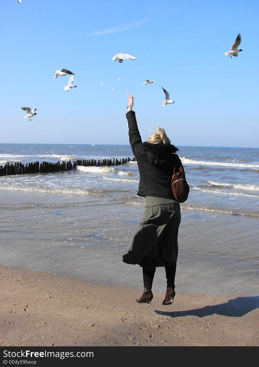 Young woman feeding seagulls on the beach in Kołobrzeg (Poland)