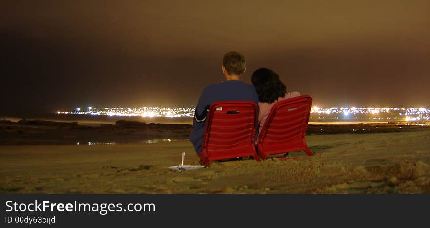 Romatic photo of couple sitting on beach, with citylights in the background. Romatic photo of couple sitting on beach, with citylights in the background.