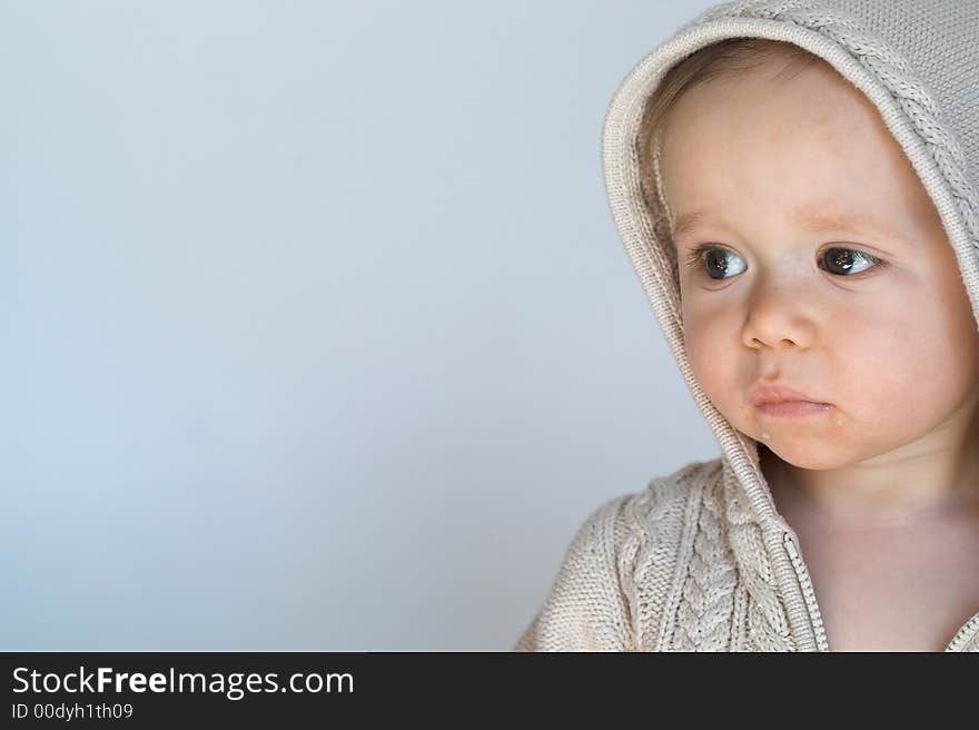 Image of cute baby wearing a hooded sweater, sitting in front of a white background. Image of cute baby wearing a hooded sweater, sitting in front of a white background