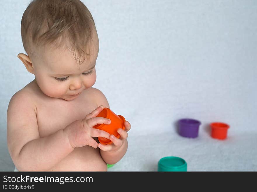 Image of adorable baby playing with stacking cups, sitting in front of a white background. Image of adorable baby playing with stacking cups, sitting in front of a white background