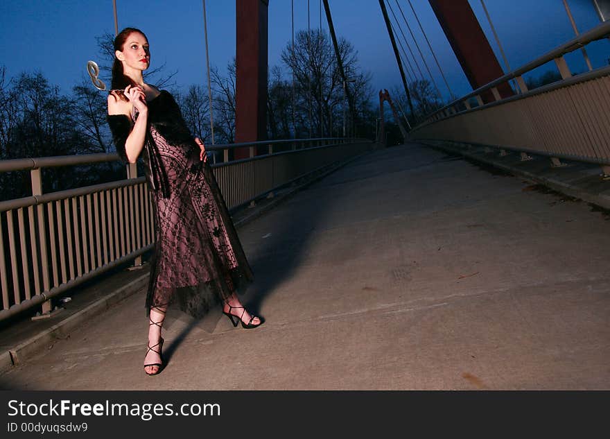 Tall female fashion model poses on a walkway at twilight. Tall female fashion model poses on a walkway at twilight.