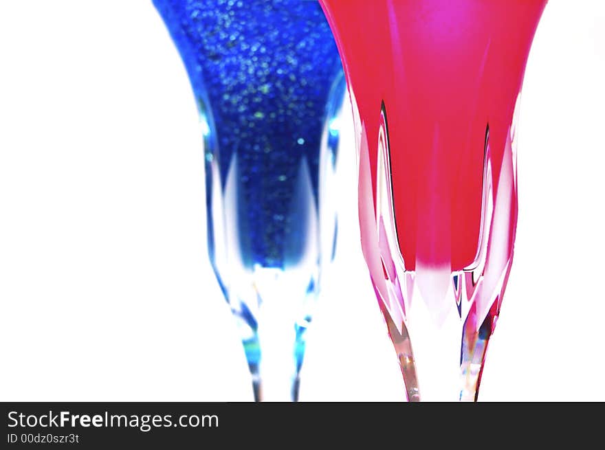 Fancy wine glasses with a swirling purple wine with sparkles in it and another glass with a bright red liquid.