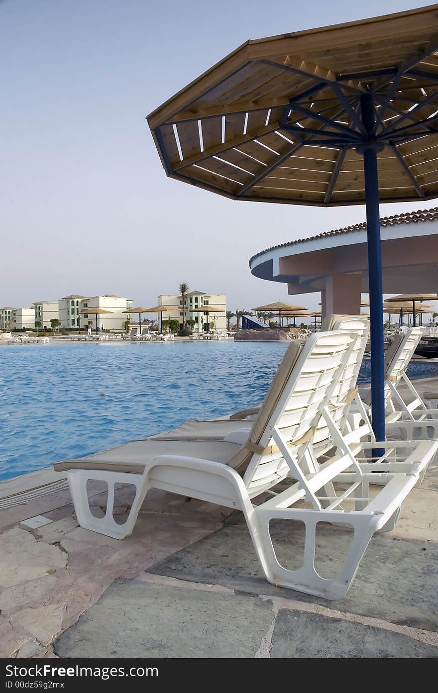 Overview at resort pool at a sunrise with chairs and umbrella at front. Overview at resort pool at a sunrise with chairs and umbrella at front