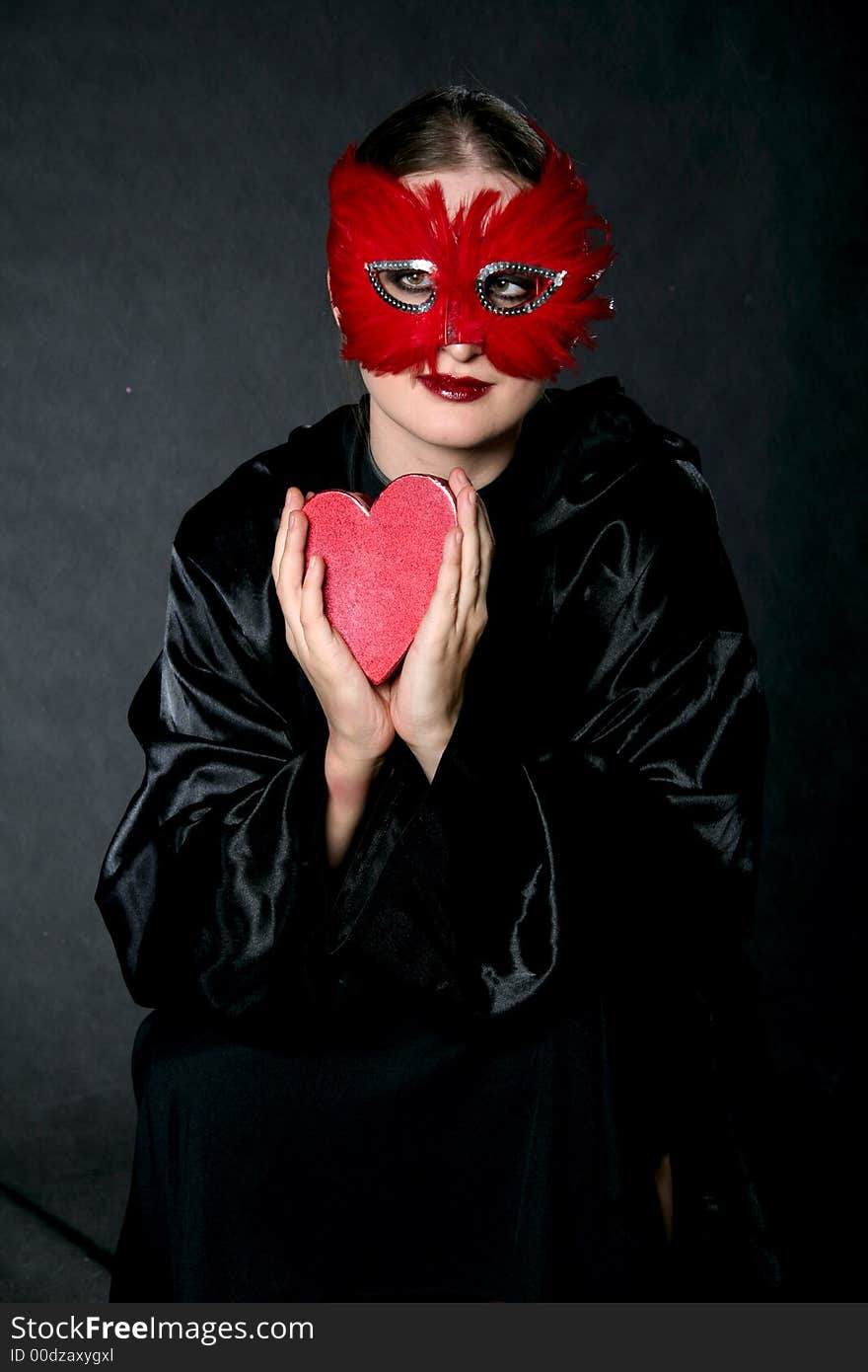 Women in red mask with heart-box in hands. Make-up black background. Women in red mask with heart-box in hands. Make-up black background.