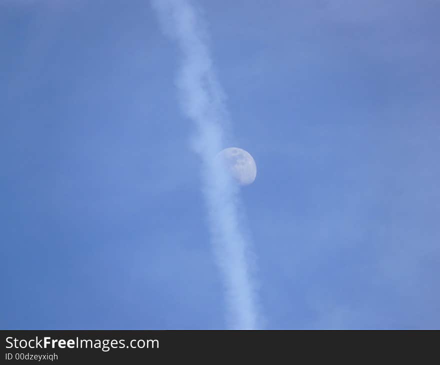 The moon half hidden behind an airplane trail, early evening. The moon half hidden behind an airplane trail, early evening