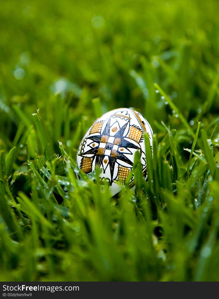 Traditional Easter Egg, painted with the symbol of the cross, on bright green grass covered with morning dew. Traditional Easter Egg, painted with the symbol of the cross, on bright green grass covered with morning dew