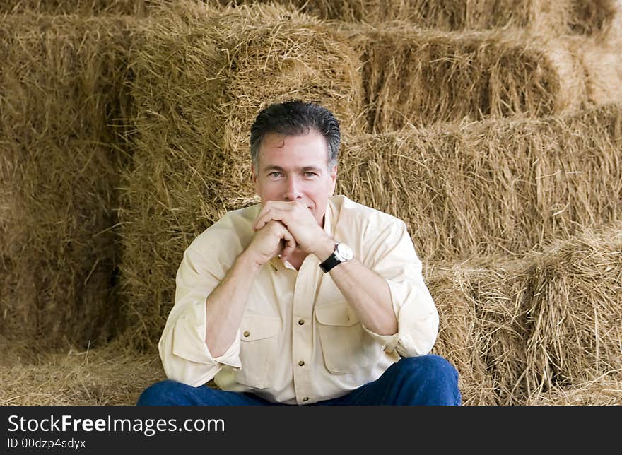 Handsome mature white male with a very contented, confident air about him sitting on stacks of fresh baled hay. Handsome mature white male with a very contented, confident air about him sitting on stacks of fresh baled hay.