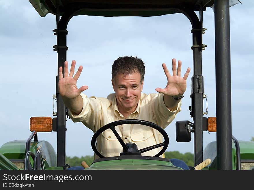 Man with a slightly worried smile sitting on a tractor gesturing with both hands in the air for something or someone to stop. Man with a slightly worried smile sitting on a tractor gesturing with both hands in the air for something or someone to stop.