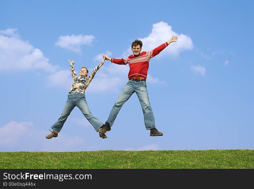 Two young people jumping on a green grass on a background of the dark blue sky with clouds. Two young people jumping on a green grass on a background of the dark blue sky with clouds