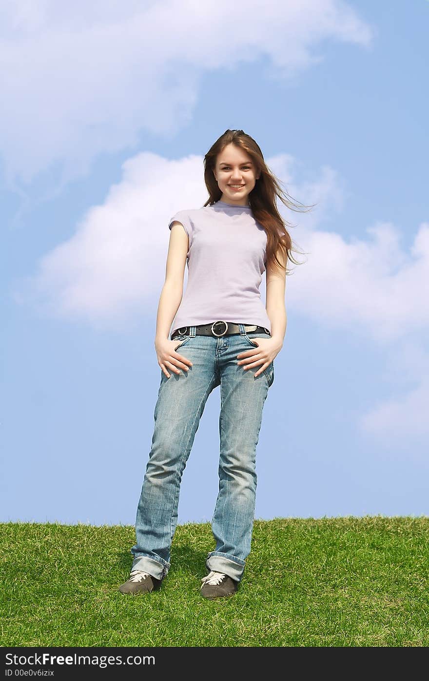 Portrait of the young pretty girl stand on a green grass on a background of the dark blue sky with clouds. Portrait of the young pretty girl stand on a green grass on a background of the dark blue sky with clouds