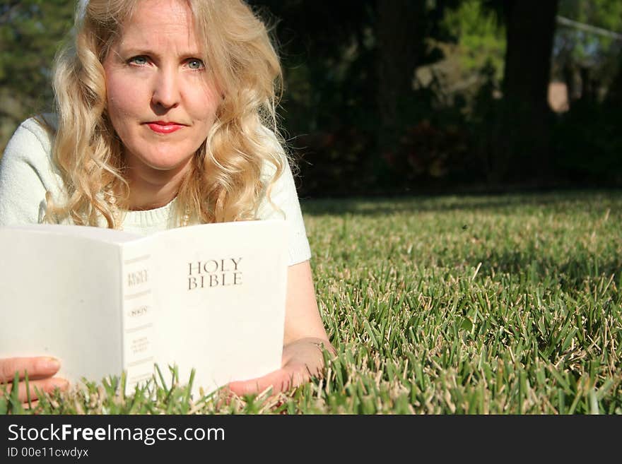 Shot of a woman reading holy bible in grass looking