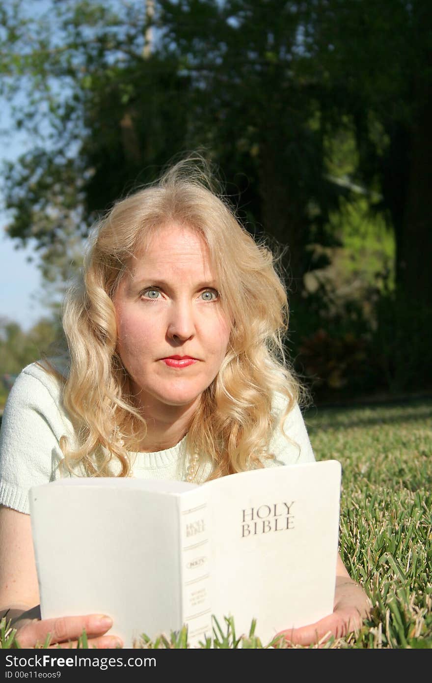 Shot of a woman reading holy bible in grass looking vertical