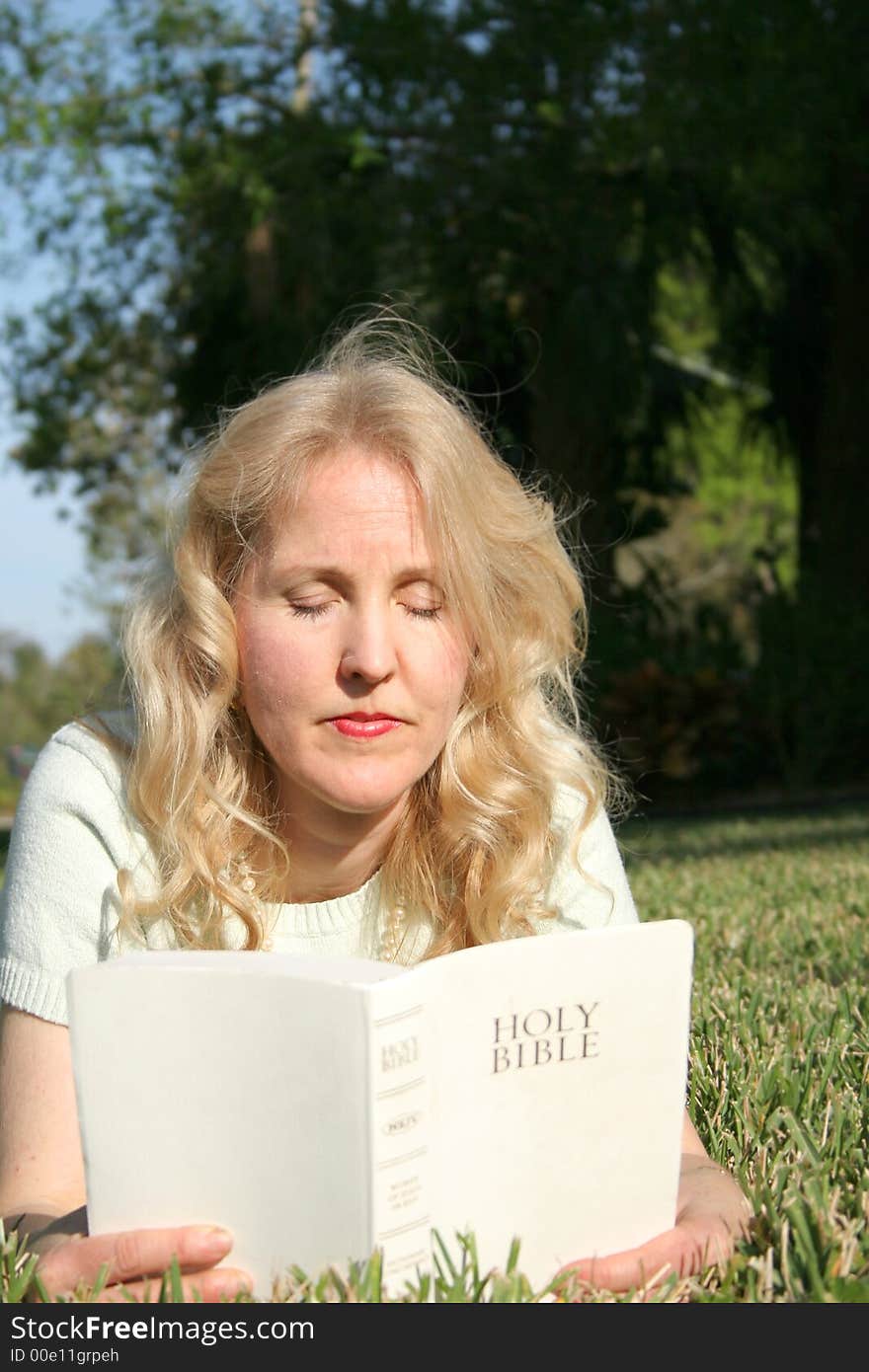 Shot of a woman reading holy bible in grass vertical