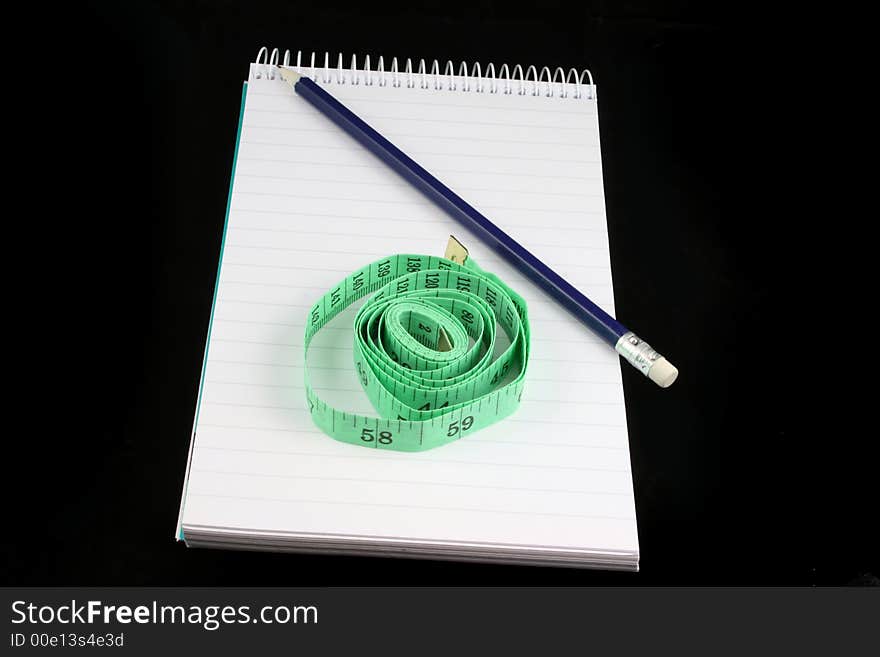 Notepad, pencil, and tape measure on a black background. Notepad, pencil, and tape measure on a black background