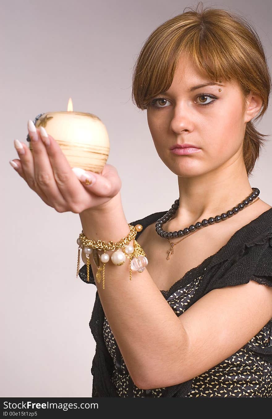 The girl looks at a candle in a hand on a grey background. The girl looks at a candle in a hand on a grey background