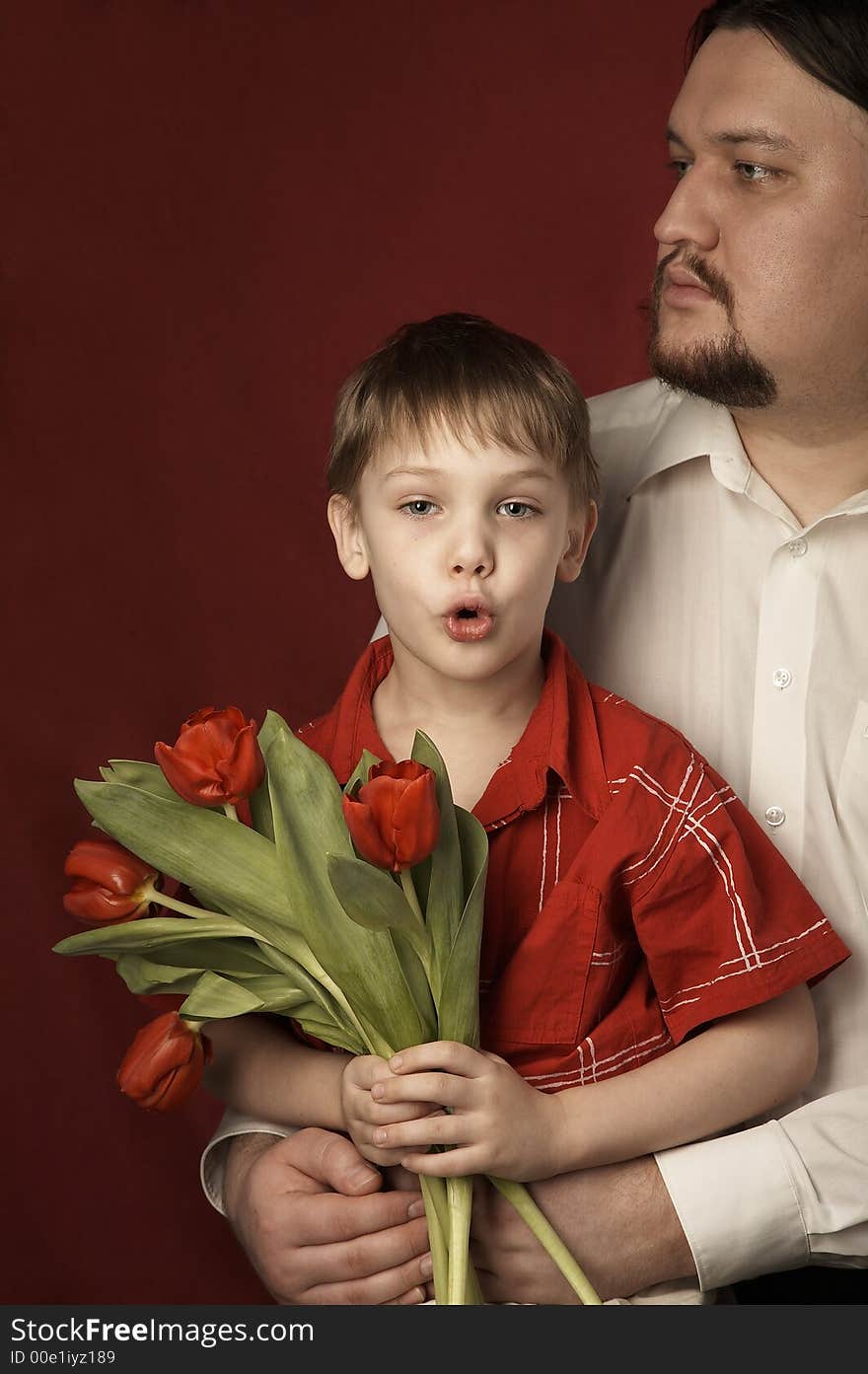 father and son in red shirt with red tulips on red background. father and son in red shirt with red tulips on red background