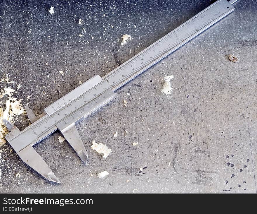 A vernier calliper gauge lying on a metal surface, some wooden shavings scattered all over the place.