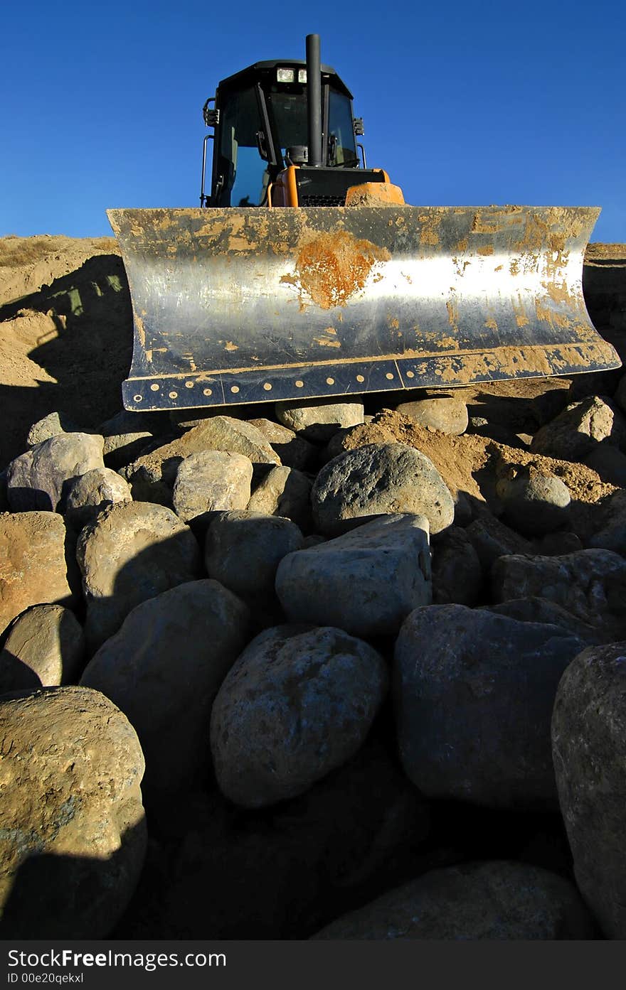 Bulldozer at construction site with boulders and blue sky