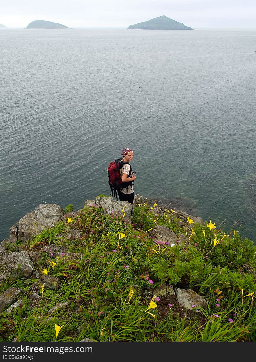 Sea coastal landscape with pretty hiking girl standing on the ocean rock with flower meadow. Sea coastal landscape with pretty hiking girl standing on the ocean rock with flower meadow