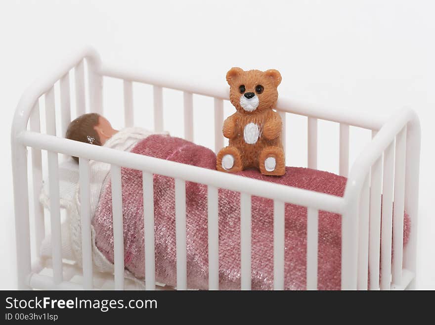 A close up of a toy sleeping child in crib bed with teddy bear, shot on white. A close up of a toy sleeping child in crib bed with teddy bear, shot on white