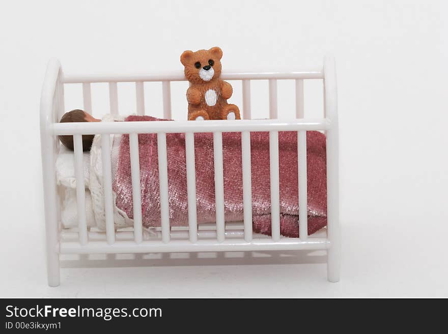 A close up of a toy sleeping child in crib bed with teddy bear, shot on white