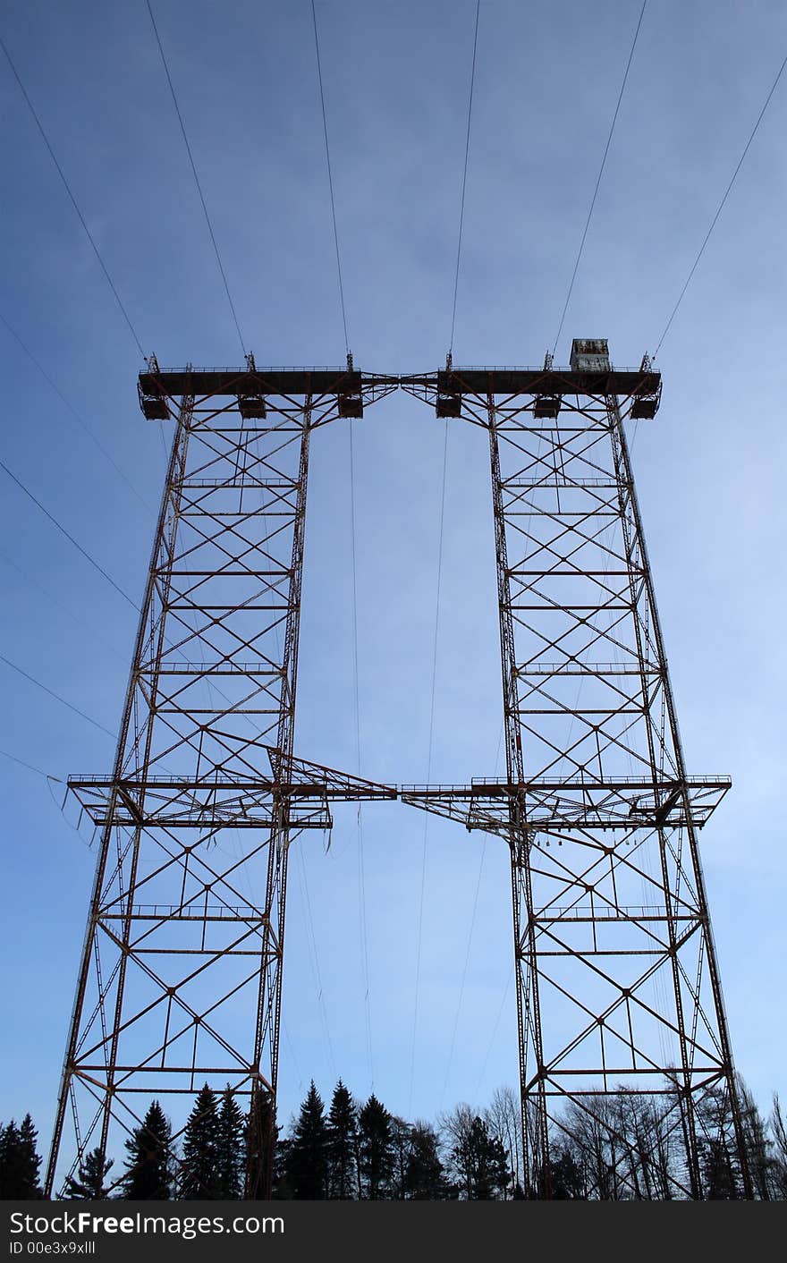 Silhouette of a big double electricity pylon in the forest.