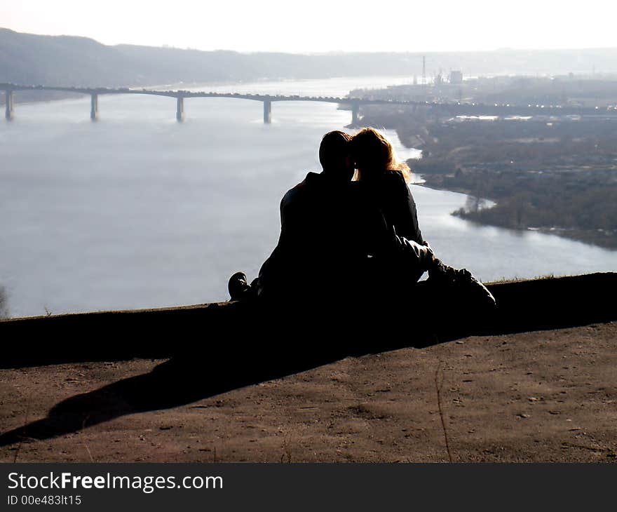 Amorous pair at a rock above a river. A time stoped. Even cars put up on the bridge