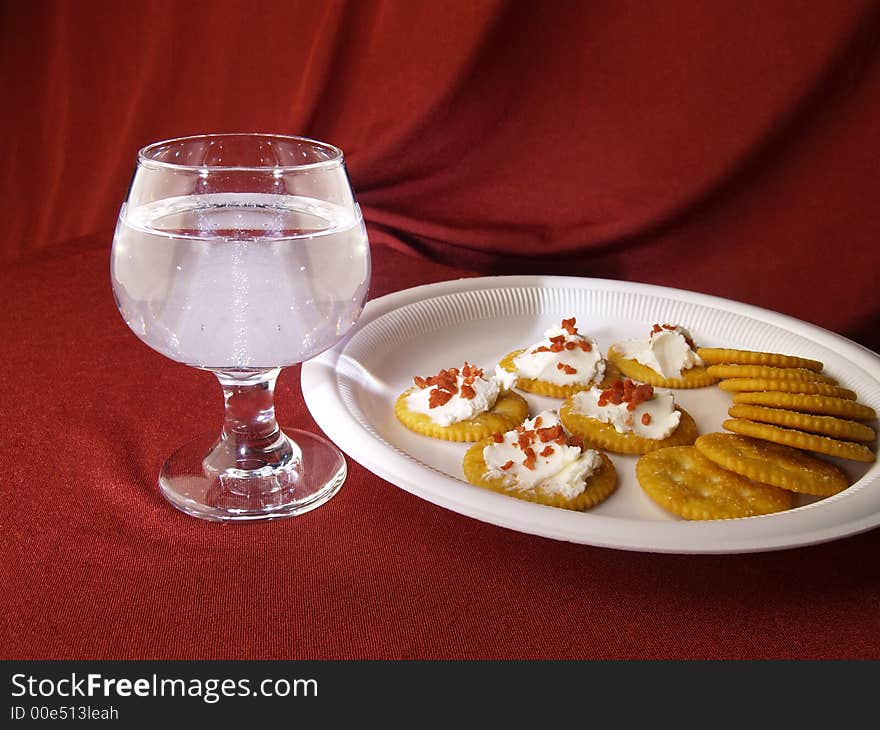 Wine glass with cracker snacks against a red drapped background.