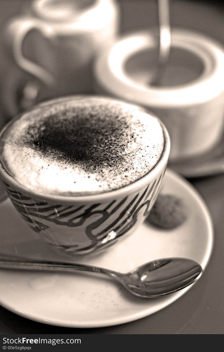 An appetizing cup of cappuccino with amaretto cookies, milk jug and powdered sugar in the background. An appetizing cup of cappuccino with amaretto cookies, milk jug and powdered sugar in the background