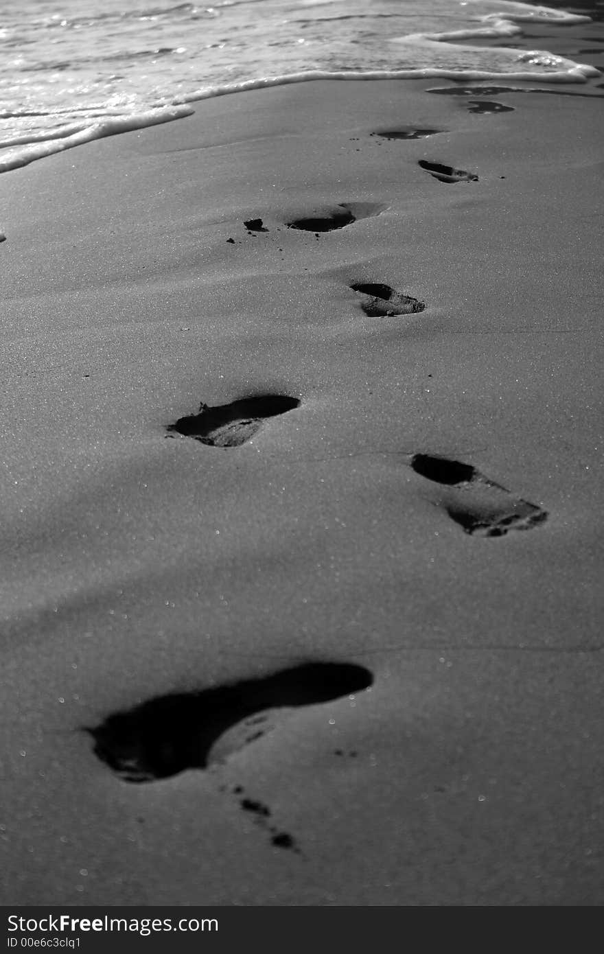 Black and white foot prints at the beach being washed away by a wave