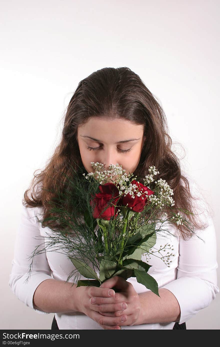 A young woman with dark hair smelling a bouquet of red roses. A young woman with dark hair smelling a bouquet of red roses